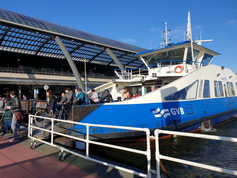 One of the city's ferries having just docked outside the Amsterdam Centraal station, with pedestrians and cyclists exiting.